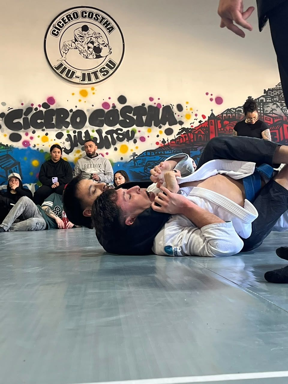 Dos competidores con kimono trabajan agarres en el suelo durante un encuentro de Jiu-Jitsu